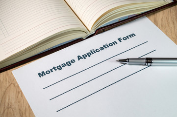 Mortgage applications form and pen on bright wooden office desk.