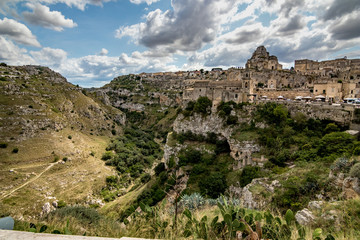 Fototapeta na wymiar Summer day scenery street view of the amazing ancient town of the Sassi with white puffy clouds moving on the Italian blue sky. Matera, Basilicata, Italy