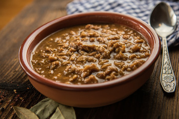 tripe stew sauce in brown ceramic pot on a wood table 