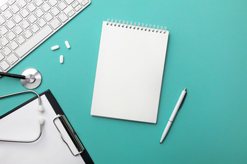 Stethoscope in doctors desk with notebook, pen, keyboard, mouse and pills