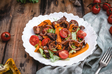 salad with roasted beef, tomatoes, lettuce and grilled pepper on white plate with fresh and grilled vegetables on brown wooden table, copy space