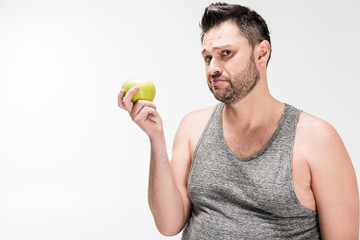 dissatisfied overweight man holding green apple and looking at camera isolated on white