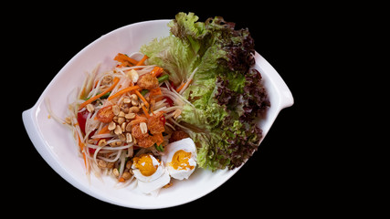 Papaya salad with salad leaves in a white plate on a black background