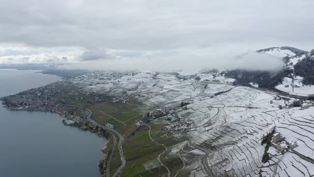 Aerial high flight over snow covered Lavaux vineyard on a foggy and cloudy day, season change between winter and spring, Switzerland