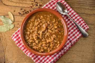 tripe stew sauce in brown ceramic pot on a wood table 