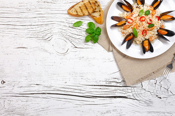 Fried rice with seafood mussels, shrimps and basil in a plate with burlap, toasted baguette and fork on white cracked wooden table