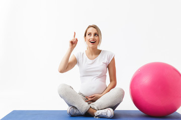 Beautiful young pregnant yoga fitness woman posing isolated over white wall background make exercises with ball.