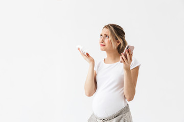 Displeased young pregnant woman posing isolated over white wall background talking by phone.