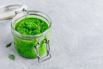Homemade basil pesto sauce in glass jar with parmesan cheese and olive oil