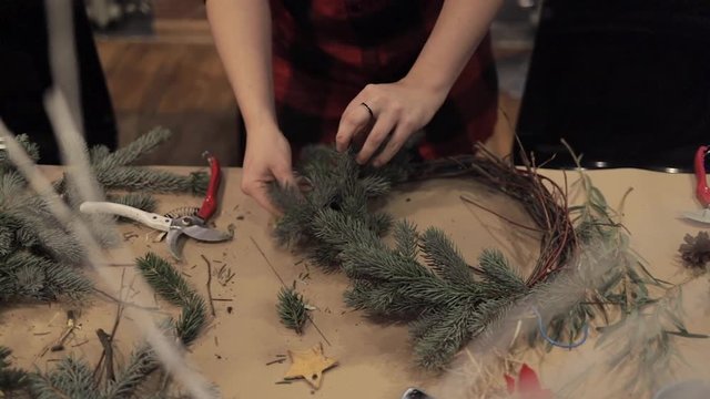 Close up of female hands arranging pine branches making christmas wreath. Pine branch base for christmas wreath. Dry branch for christmas wreath decoration handmade at studio