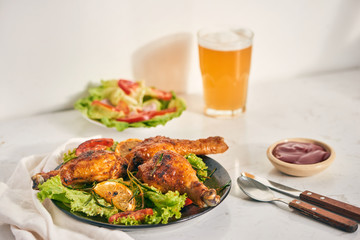 Grilled chicken legs roasted on the grill on dark plate with tomato sauce in a bowl and lettuce leaves, glass mug of beer