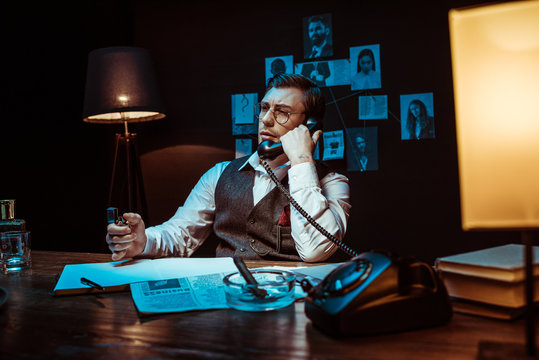 Pensive Detective In Glasses Talking On Telephone In Dark Office