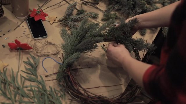 Close up of female hands tightening up pine branches with wire making christmas wreath. Pine branch base for christmas wreath. Dry branch for christmas wreath decoration handmade at studio