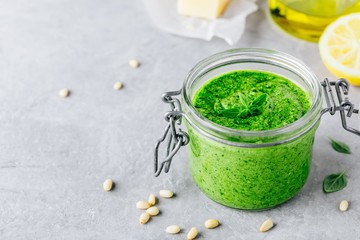 Homemade basil pesto sauce in glass jar with parmesan cheese and olive oil