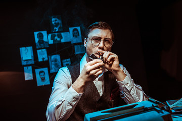 Pensive detective in glasses lighting cigar in dark office