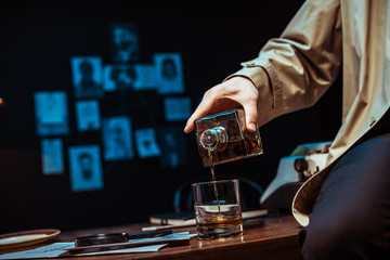 Partial view of detective pouring cognac in glass while sitting on table