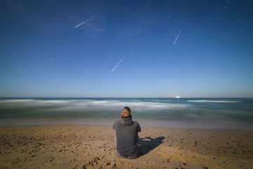 Young man on the Baltic seashore watching the meteor shower late at night