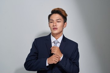 Confident businessman straightening his tie over gray background and looking at camera