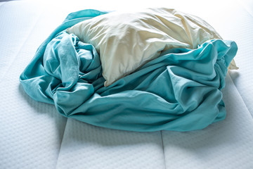 Turquoise crumpled bed sheet with ivory pillow on white bed, Close up shot, Selective focus, Bedroom cleaning concept