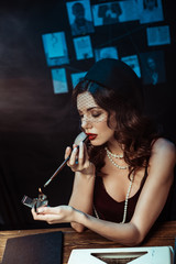 Beautiful woman with mouthpiece lighting cigarette with lighter in dark office