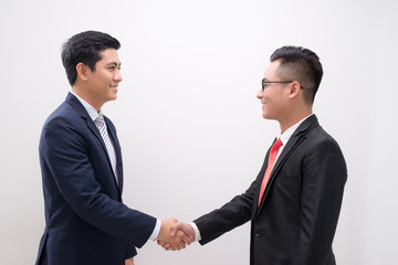Side view of two smiling young businessmen shaking hands in white background
