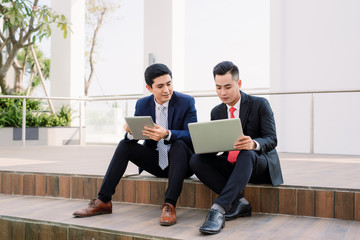 two asian business executives using ipad in city park.