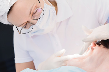Fototapeta premium Female dentist with an assistant examines the patient's mouth of a man of an aged man. High key professional work of a dentist in the dental clinic