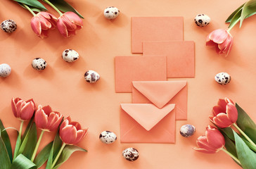 Easter flat lay on orange paper with tulips, quail eggs and greeting cards