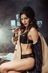 Obraz na płótnie Canvas Sexy woman in underwear and trench coat holding mouthpiece while sitting on table in office