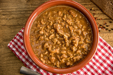 tripe stew sauce in brown ceramic pot on a wood table 