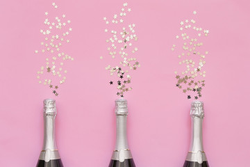 Three Champagne bottles with confetti stars on pink background. Copy space, top view