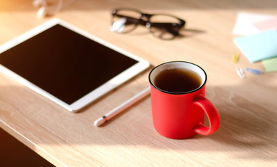 Wooden Desk. White tablet with black-rimmed glasses. Cup of tea.