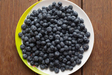 fresh blueberries closeup with dew drops on a plate on a wooden background