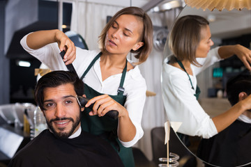 woman hairdresser shaving hair of smiling man
