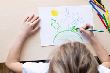 A girl draws with pencils a green house planet car wind power plants. Concept of ecology and...