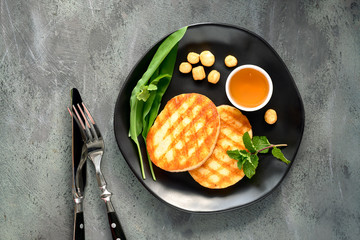 Grilled round slices of Greek cheese with honey, fresh mint and coriander leaves. Flat lay on dark...