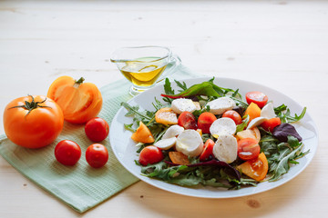 Fresh salad with arugula, cherry tomatoes, mozzarella cheese and olive oil on white wooden background