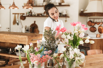 Beautiful happy young student girl posing indoors near flowers talking by mobile phone.