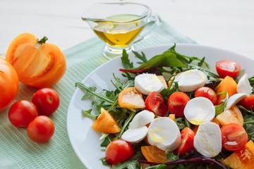 Obraz na płótnie Canvas Fresh salad with arugula, cherry tomatoes, mozzarella cheese and olive oil on white wooden background