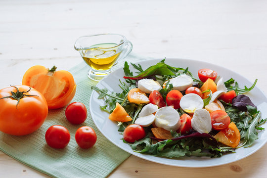 Fresh salad with arugula, cherry tomatoes, mozzarella cheese and olive oil on white wooden background