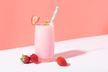 Strawberry smoothie in glass with straw and scattered berries on pink background.
