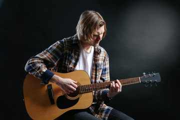 Obraz premium Handsome young man playing guitar on dark background