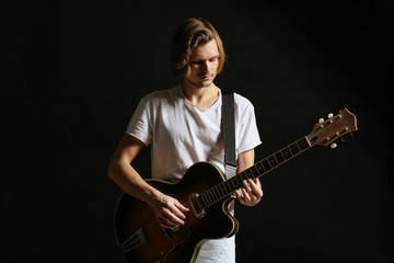 Handsome young man playing guitar on dark background