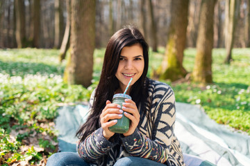 Happy healthy eating girl drinking green smoothie detox outdoors in the wood. Woman on weight loss diet vegan nutrition cleanse.