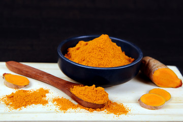 Fresh organic Turmeric powder in a bowl with slices of turmeric root