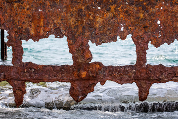 A closeup and detailed view of an old rusting ship wreckage in the ocean showing weathered holes in...