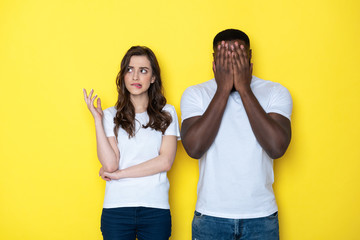 Sad young interracial couple in white T-shirts posing for camera in studio