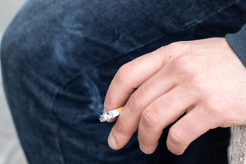 A closeup view of smoke coming from a cigarette in the hand of a Caucasian person, bad health and...