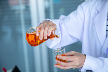 Close up scientist hand pouring orange liquid