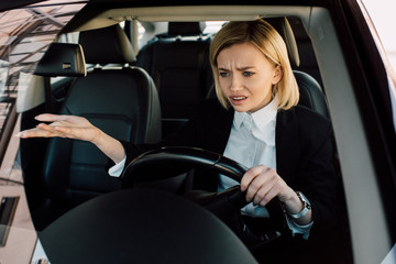 upset blonde girl holding steering wheel while gesturing and driving car